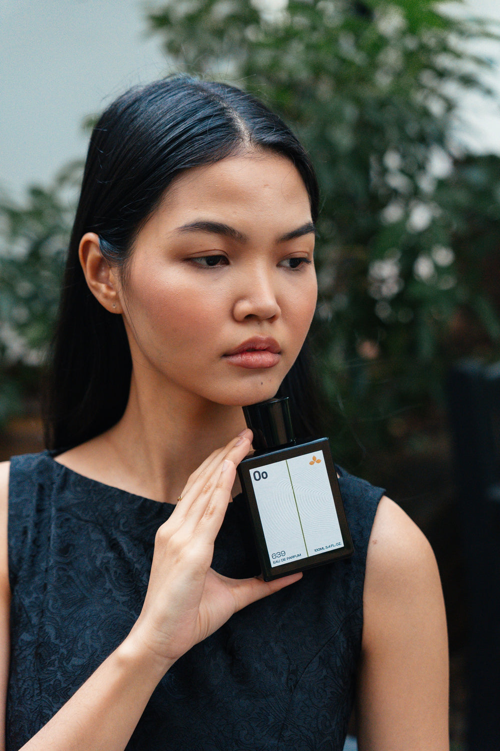 Portrait of a woman against green foliage holding perfume 639 Balance