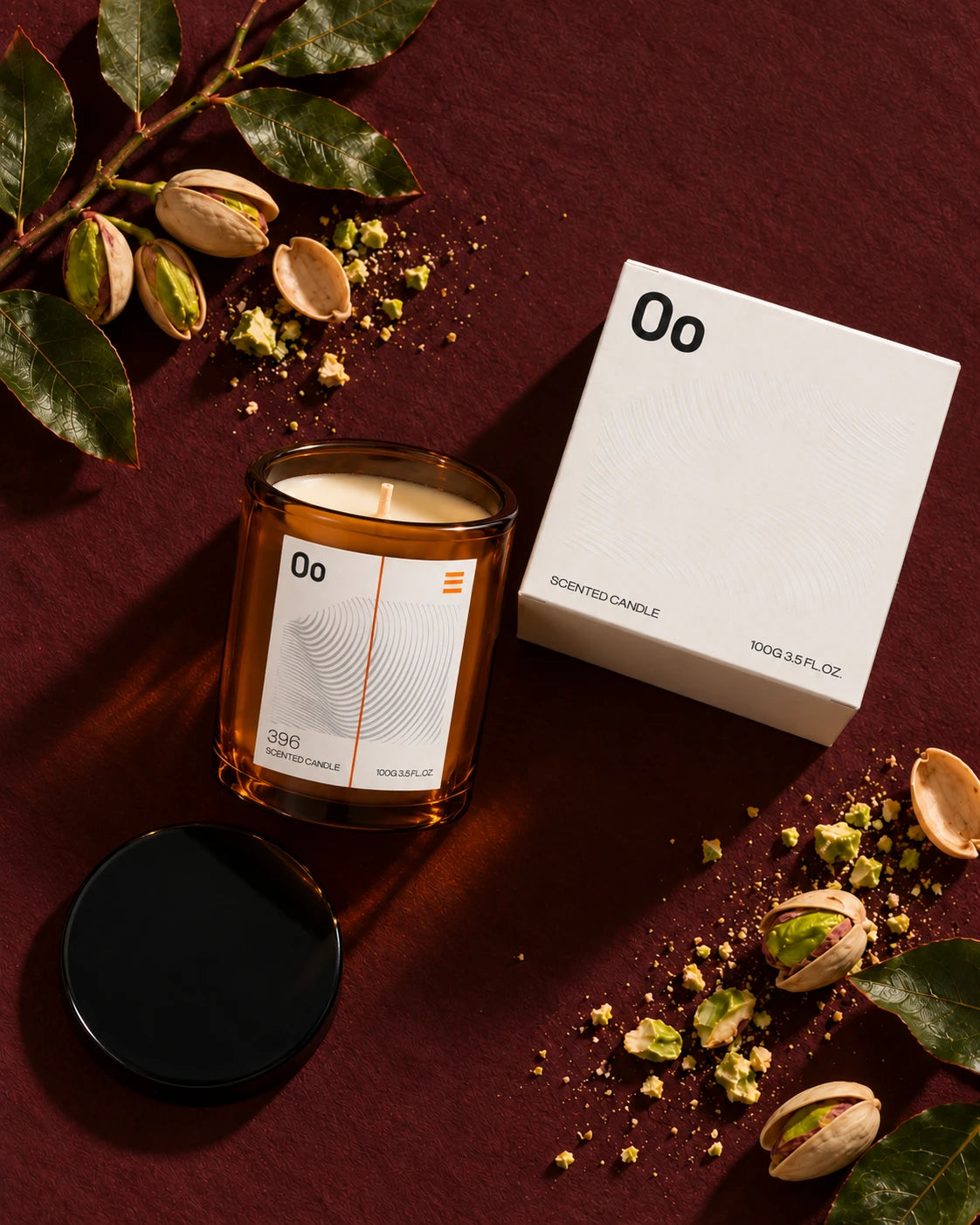 Oo La Lab amber candle and ivory gift carton on oxblood fabric, with pistachios and leaves